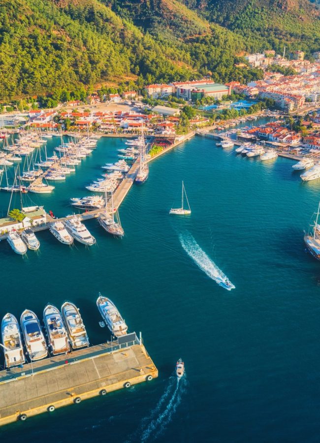 Aerial view of boats and yachts at sunset in Turkey. Colorful landscape with boats in marina bay, sea, mountains, forest, blue sky. Top view from drone of harbor with luxury yacht, sailboat. Travel